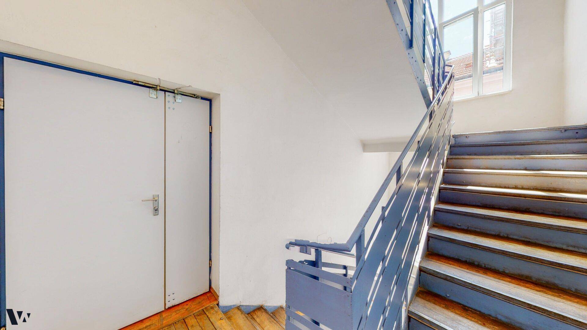 Treppenhaus mit blauen Metallgeländern und einer großen Doppeltür, die zu einem anderen Bereich führt.