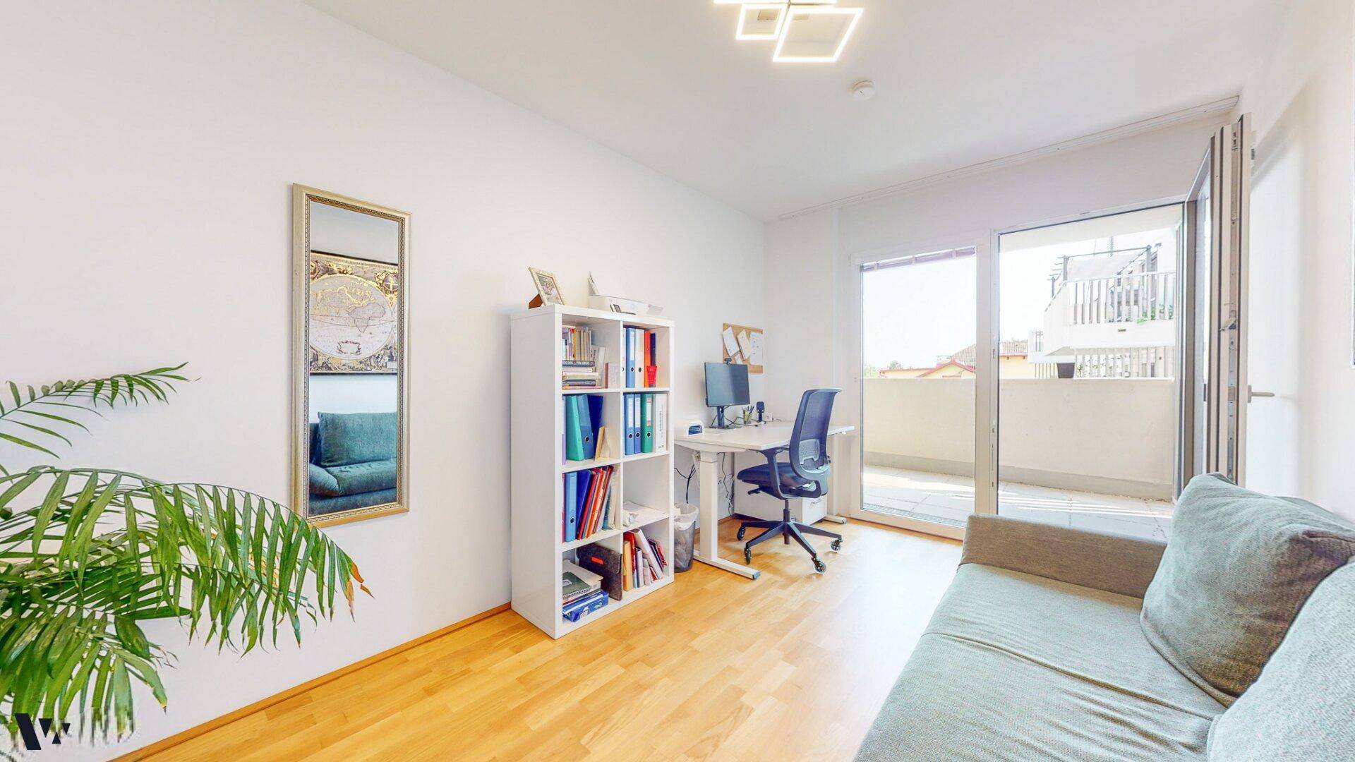 Heller Arbeitsbereich mit Schreibtisch, Bücherregal und viel Tageslicht durch die Balkontür.