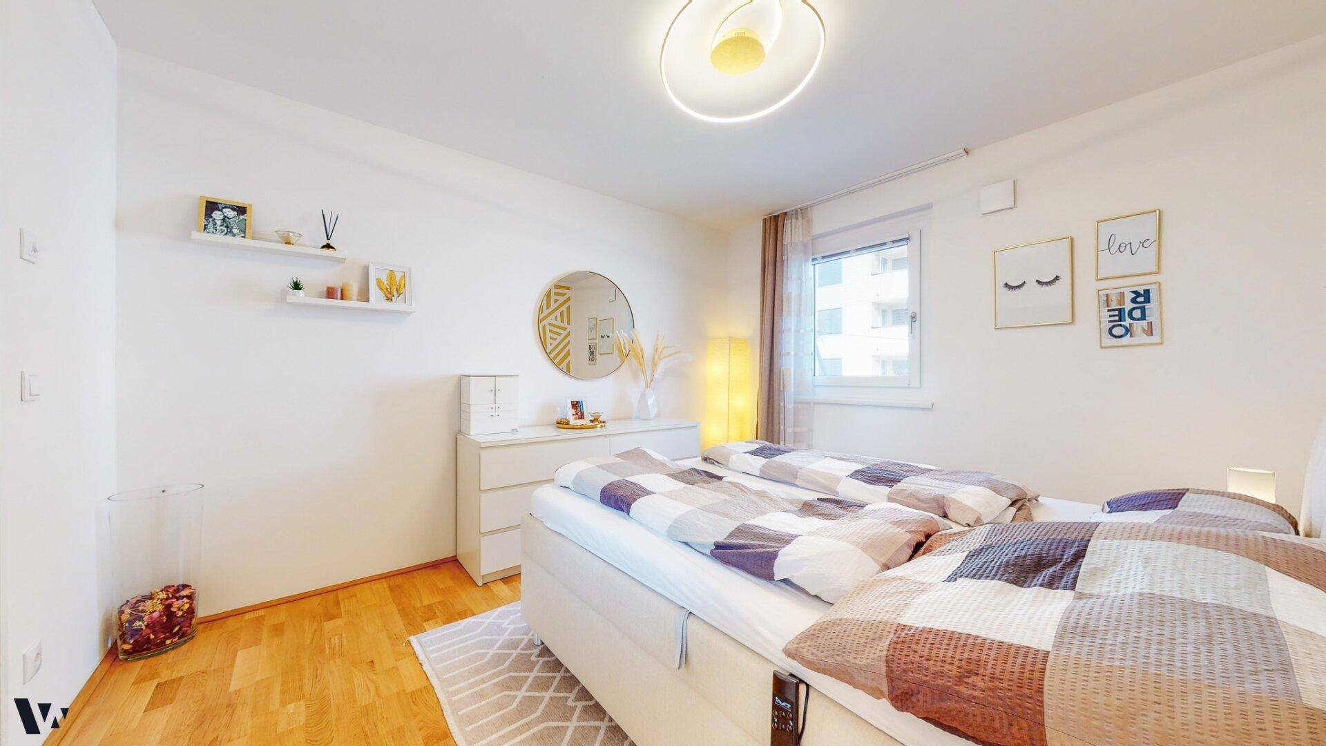 Helles Schlafzimmer mit bequemen Bett, Nachttischen und einem runden Spiegel.