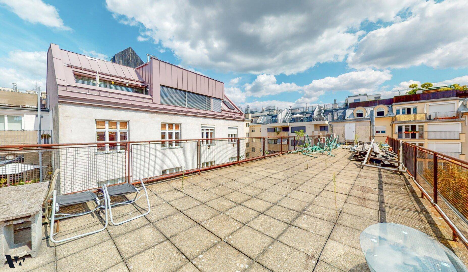 Große Dachterrasse mit Fliesenboden, Sitzgelegenheiten und Blick auf die umliegenden Gebäude.