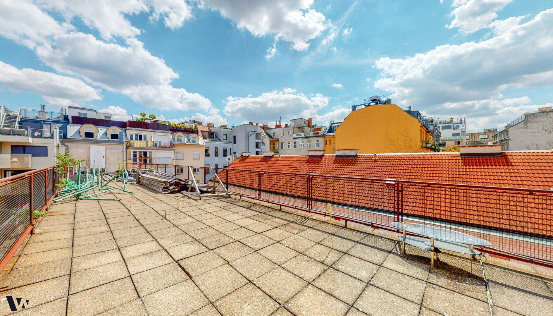 Weitläufige Dachterrasse mit Fliesenboden und Panoramablick über die Dächer der Stadt.