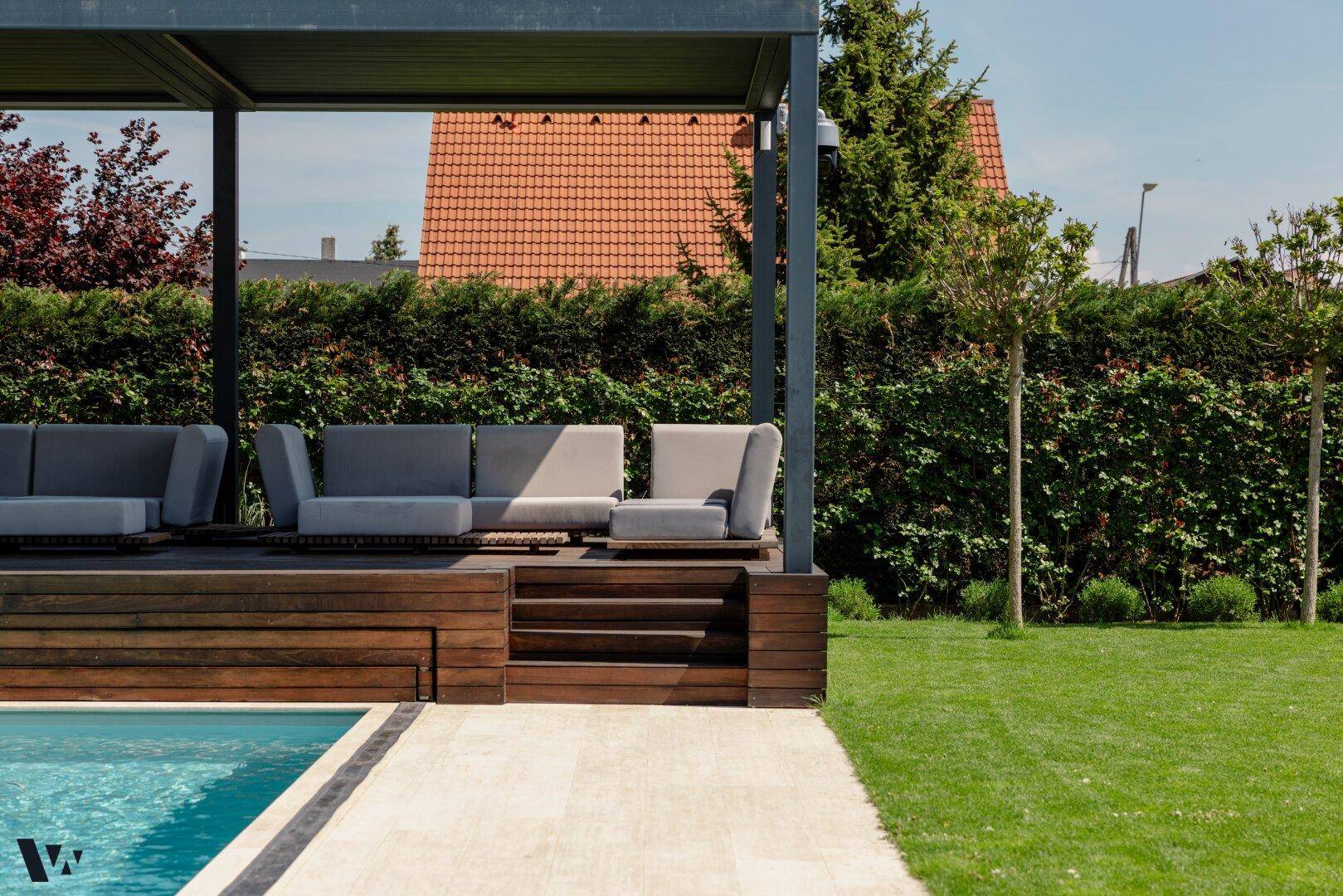Detailansicht des überdachten Lounge-Bereichs am Pool mit stilvollen Outdoor-Möbeln und Holzdeck.