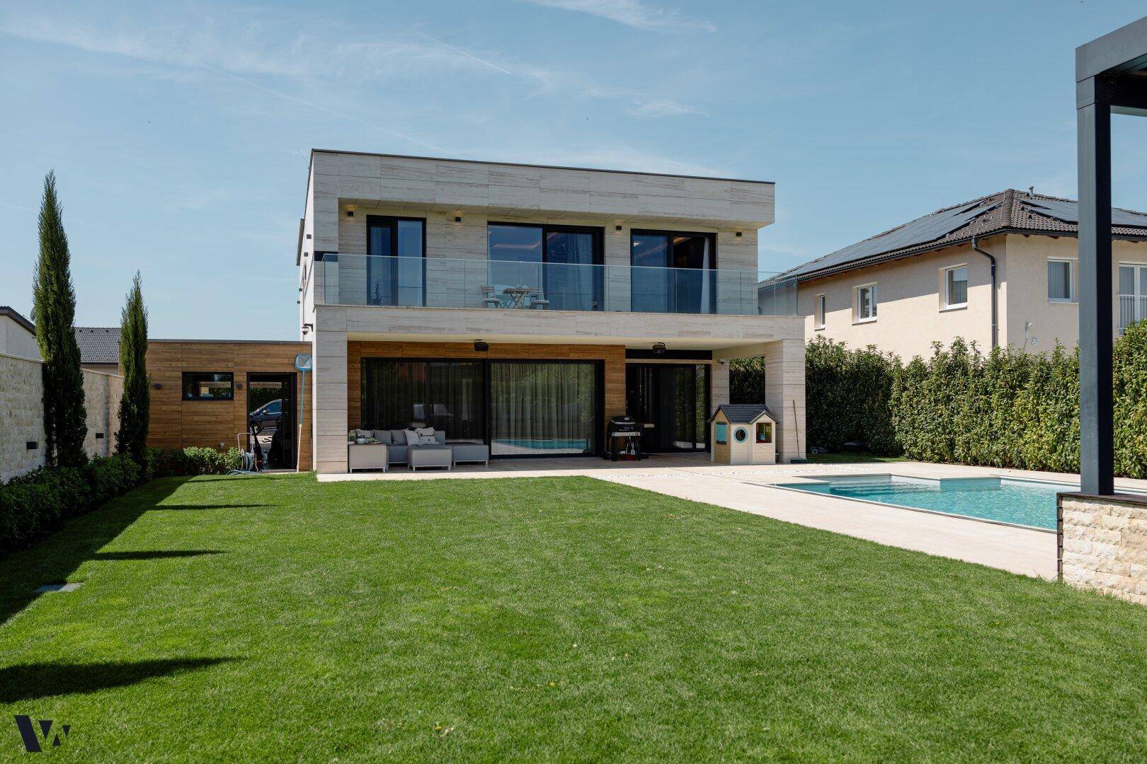 Weitläufiger Gartenbereich mit modernem Haus, Pool und gepflegter Rasenfläche unter blauem Himmel.