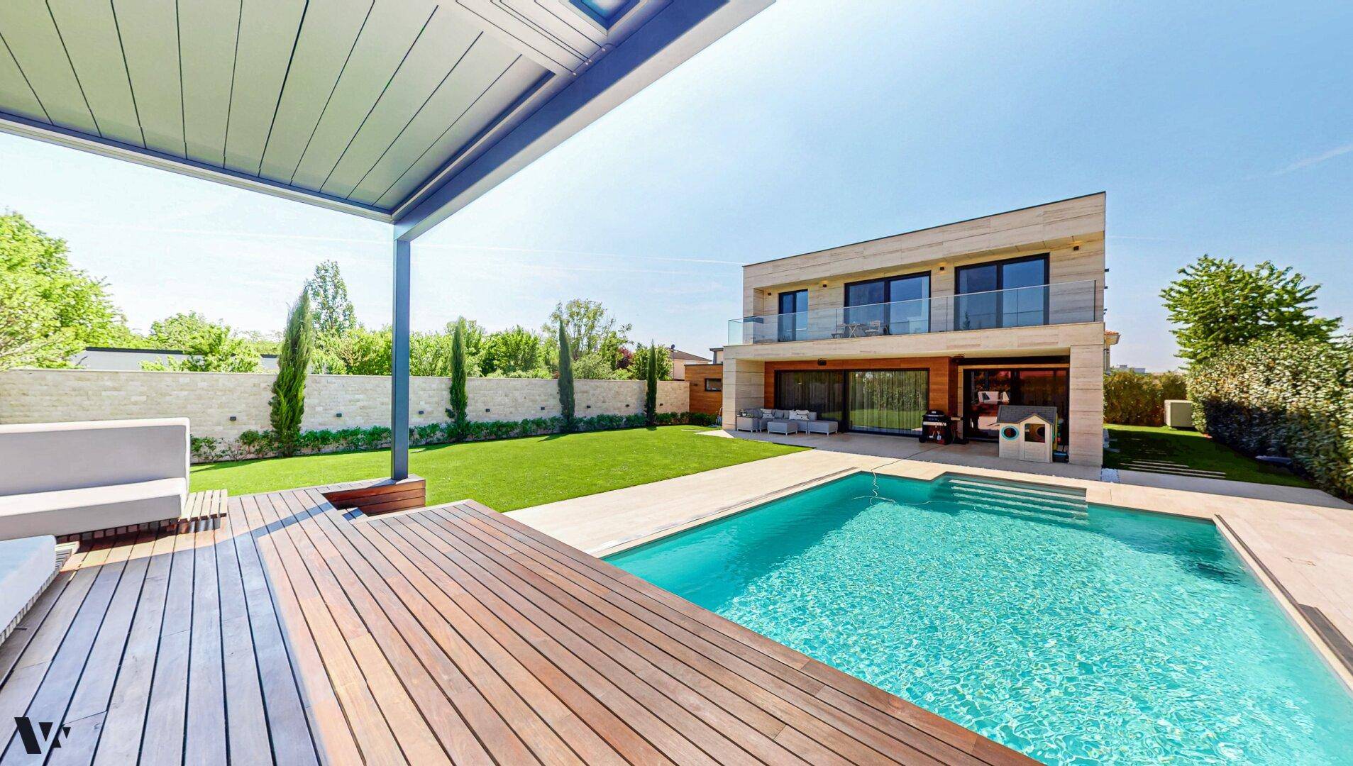 Blick von der Holzterrasse auf den modernen Pool und das stilvolle Haus mit großem Garten.