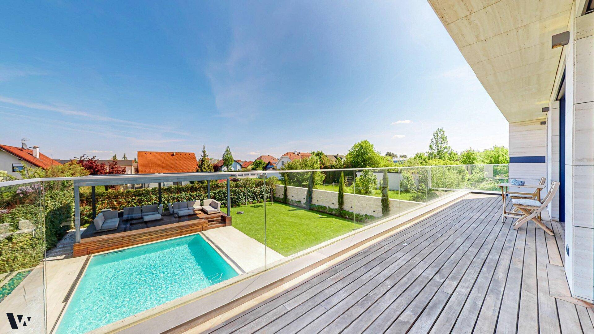 Geräumiger Balkon mit Glasgeländer bietet weiten Blick auf den Pool und den gepflegten Garten.
