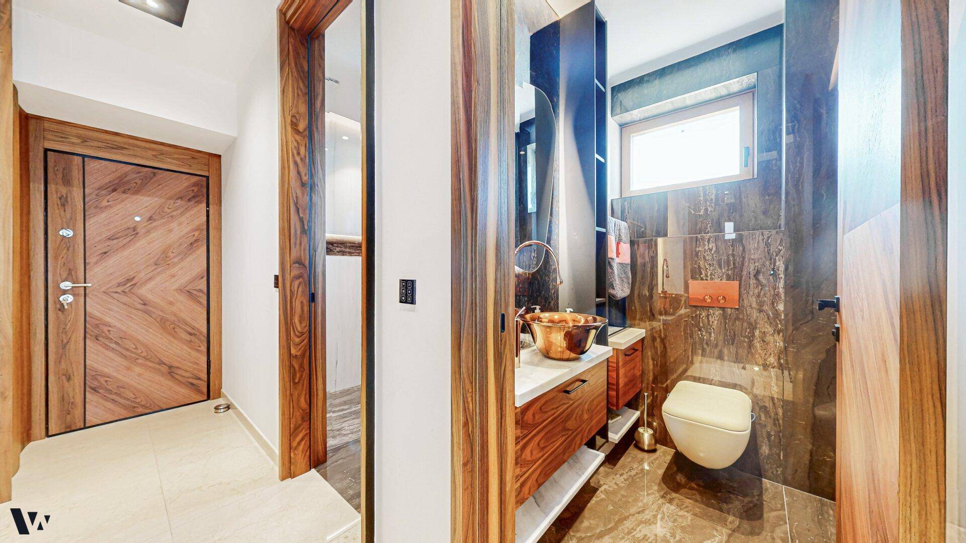 Elegantes Gäste-WC mit dunklen Marmorfliesen, Holzdetails und modernem Waschbecken.