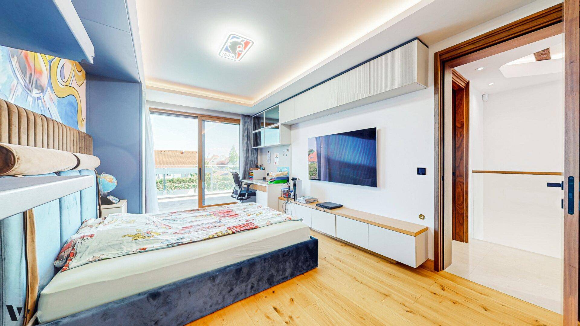 Helles Kinderzimmer mit integrierten Schränken, Schreibtisch und Fernseher an der Wand.