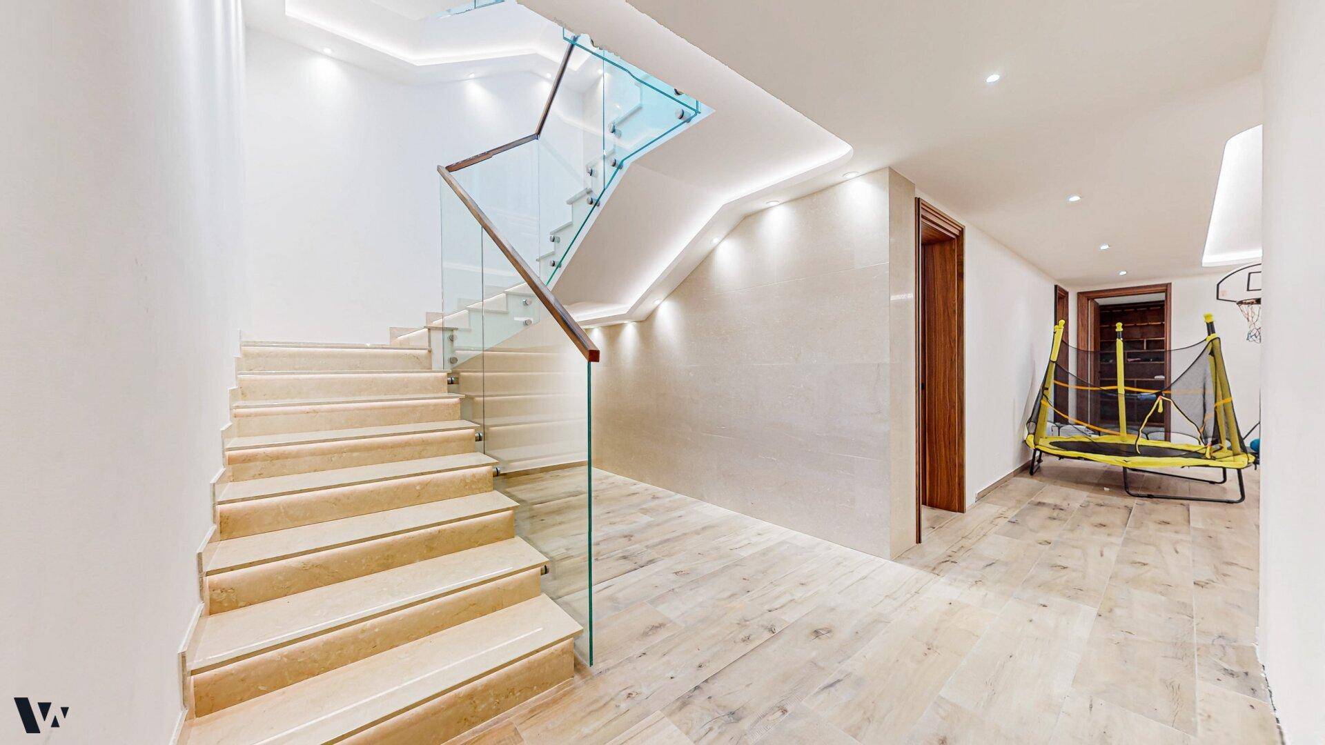 Heller Flur mit moderner Treppe aus Stein und Glasgeländer, führt zu weiteren Räumen.
