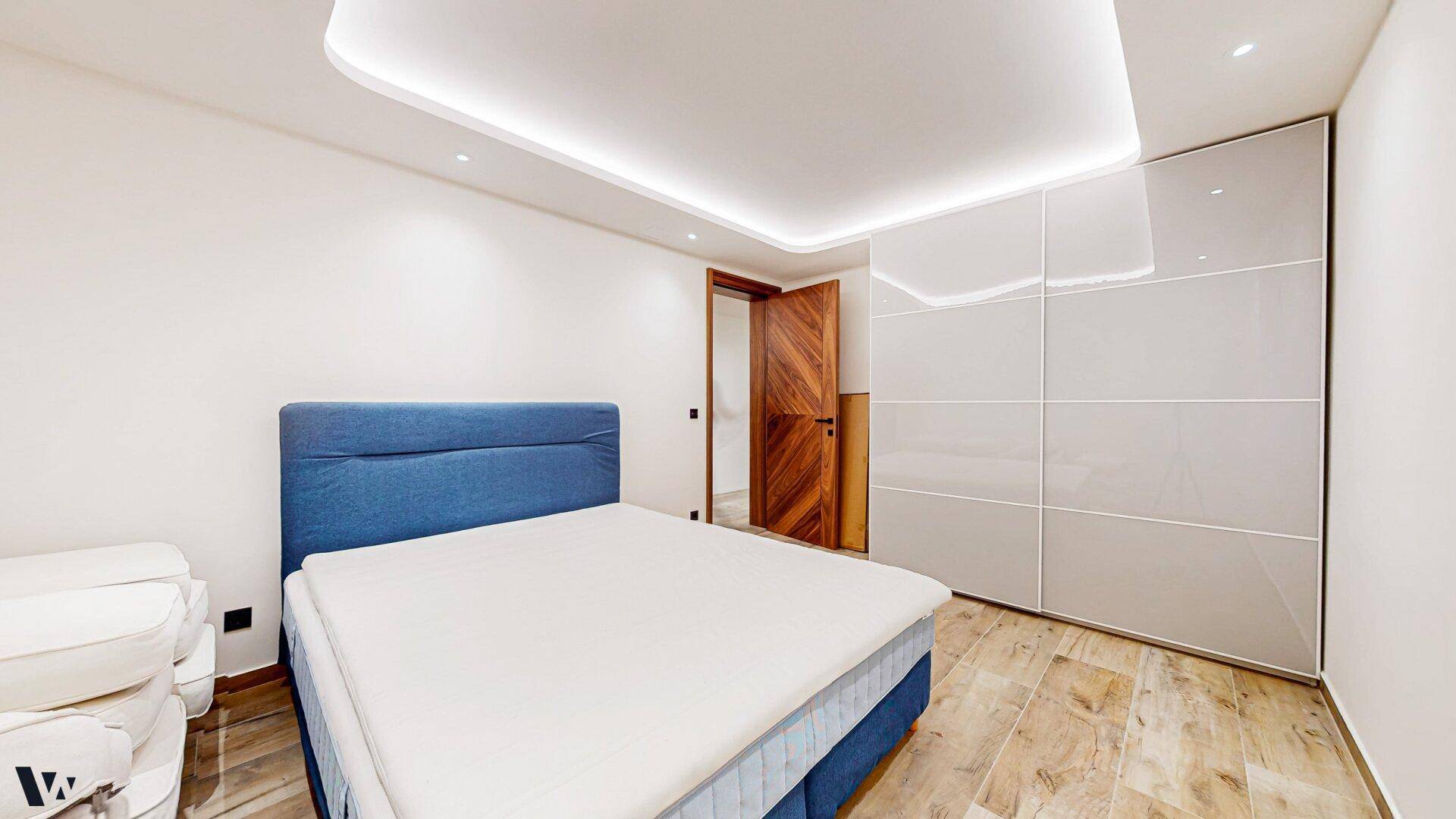 Modernes Schlafzimmer mit blauem Bett, weißen Einbauschränken und Holzboden.