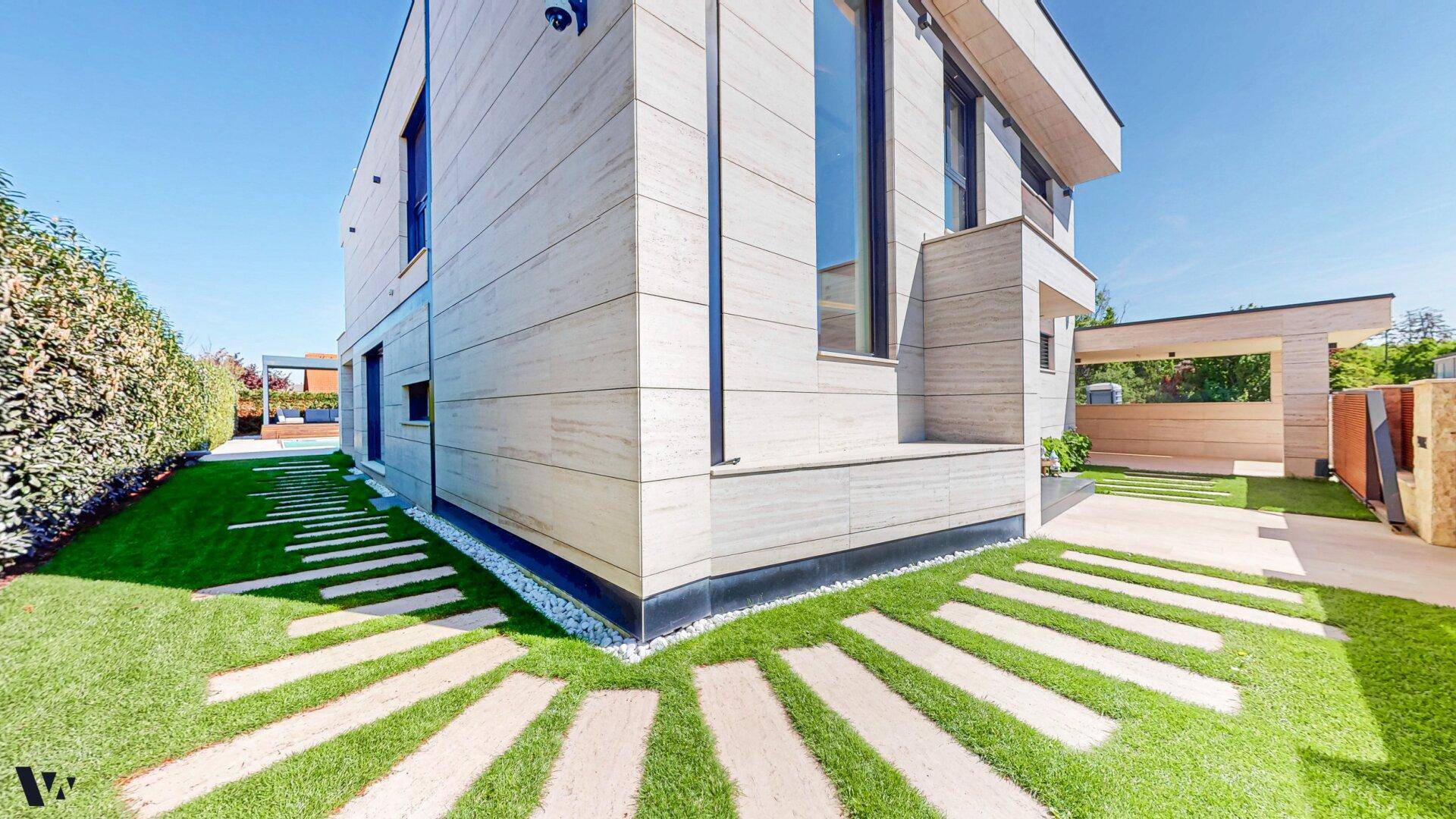 Moderne Hausfassade mit gepflegtem Rasen, Trittsteinen und üppiger Hecke.