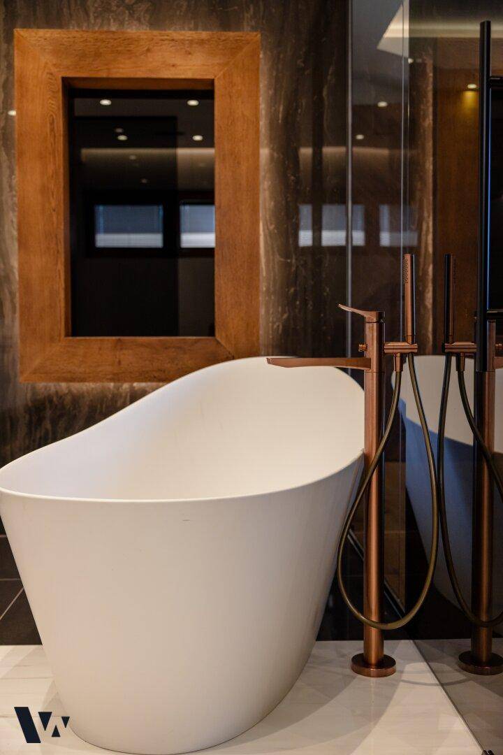 Freistehende Badewanne mit eleganten kupferfarbenen Armaturen in einem luxuriösen Badezimmer.