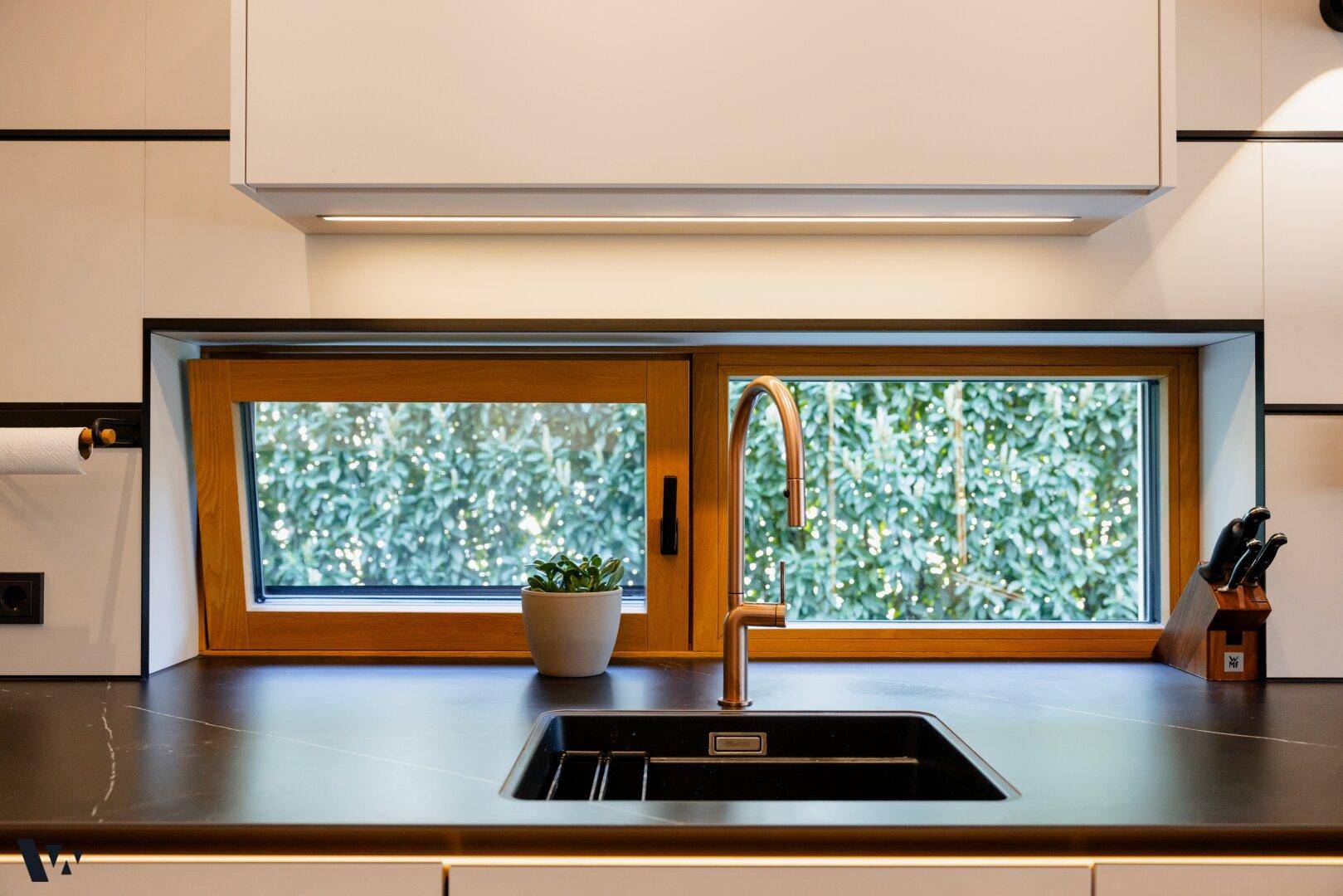 Detailansicht der modernen Küchenspüle mit schwarzem Becken und kupferfarbenem Wasserhahn.