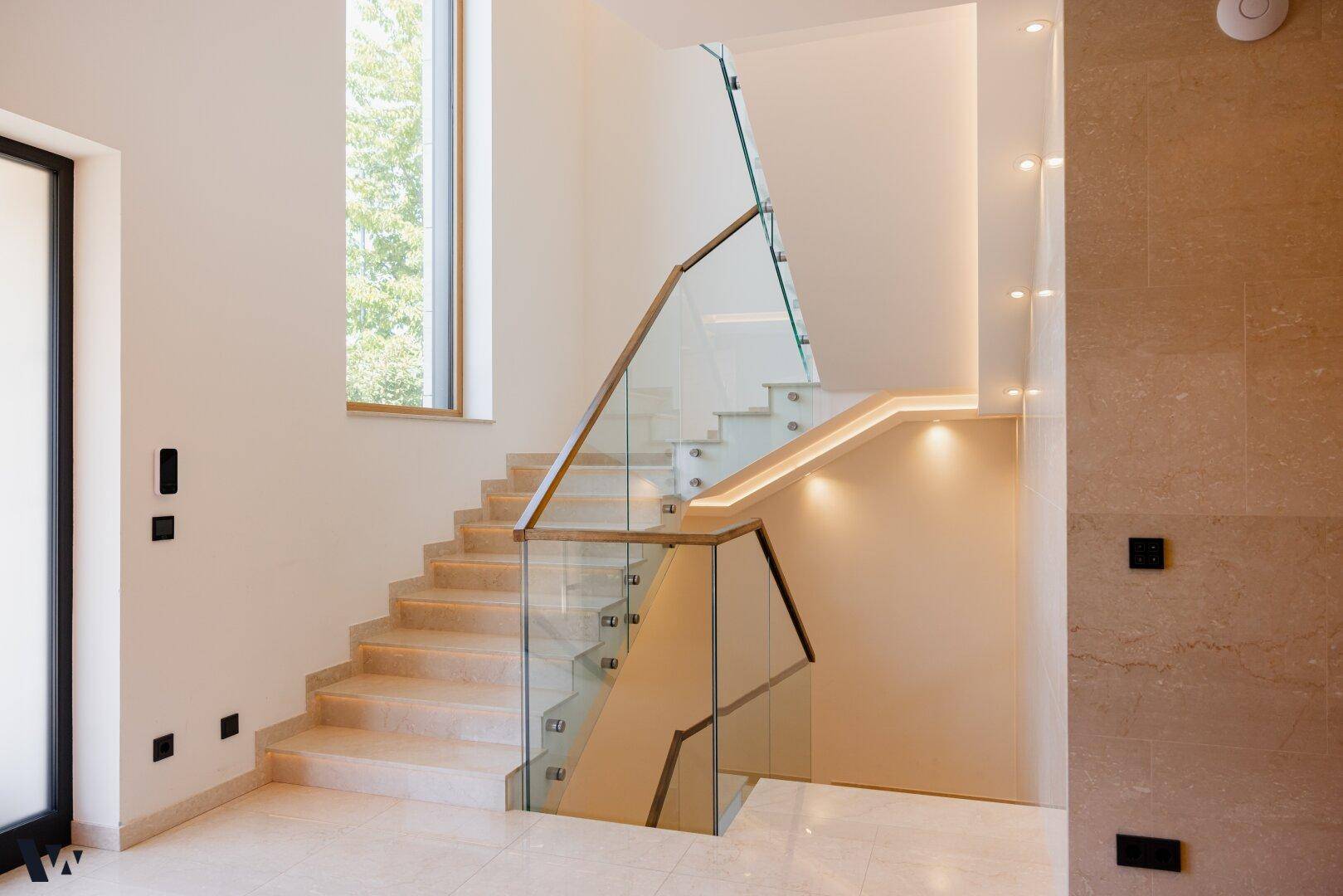 Elegante Treppe mit Glasgeländer und indirekter Beleuchtung, die die oberen Etagen verbindet.
