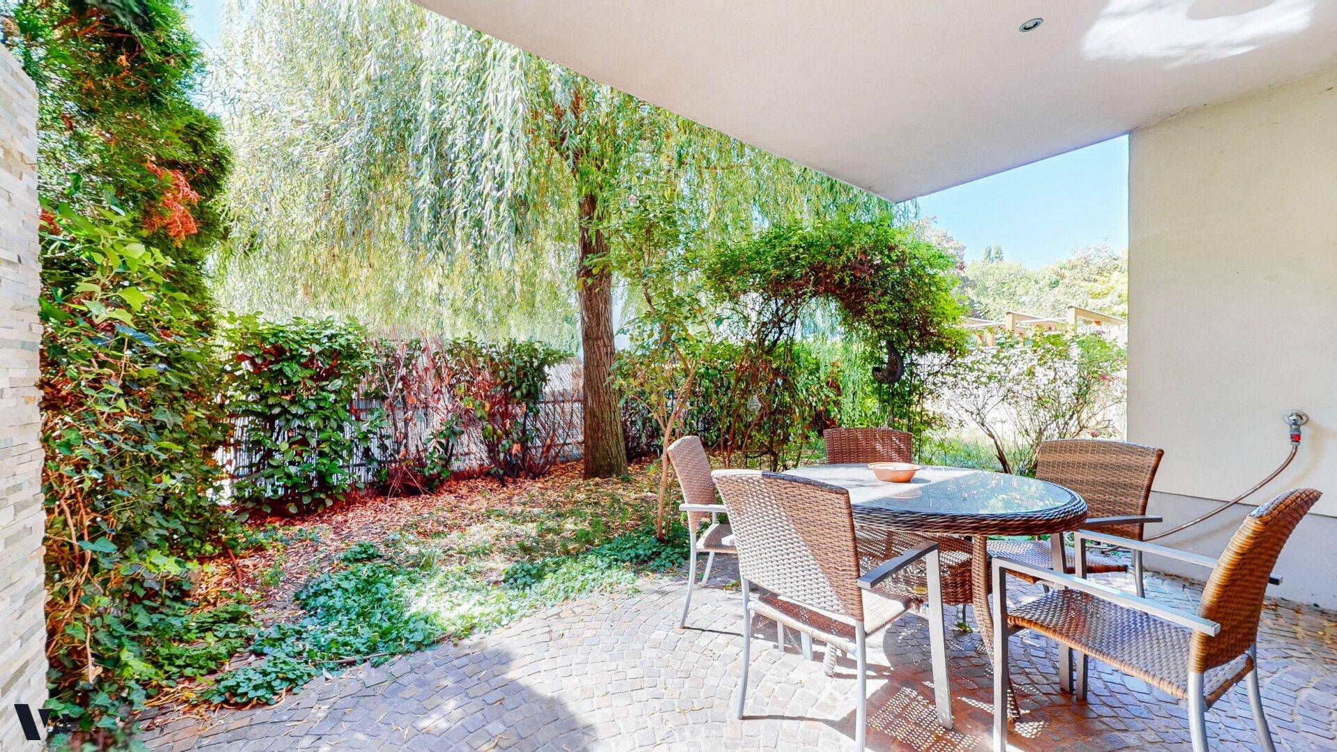 Gemütliche, überdachte Terrasse mit Sitzgelegenheiten und üppiger Bepflanzung im Garten.