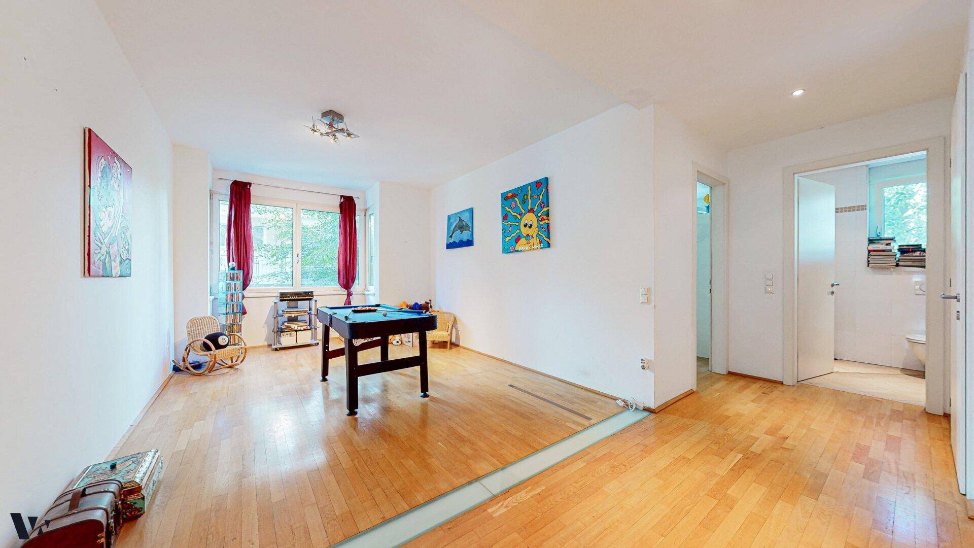 Heller Raum mit Holzboden, Billardtisch und Zugang zu einem Badezimmer.