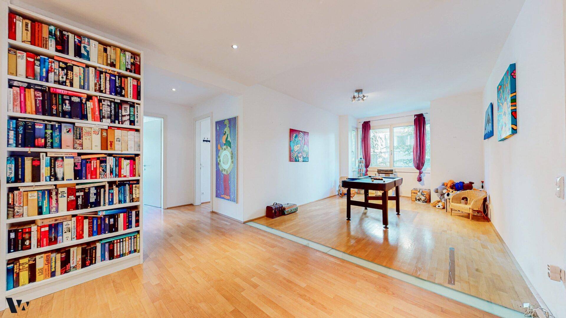 Geräumiger Raum mit Holzboden, großer Bücherwand und Billardtisch.