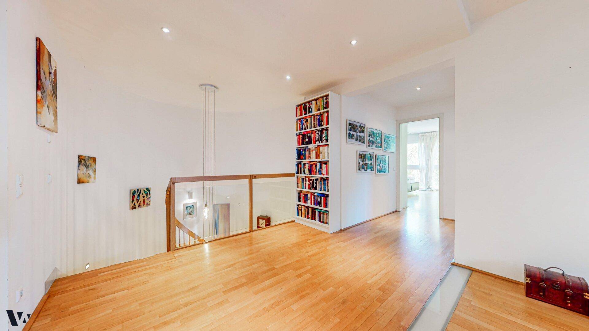 Heller Flur im Obergeschoss mit Holzboden, Bücherregal und Blick auf die untere Etage.