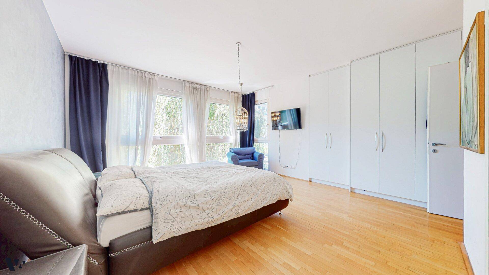 Geräumiges Schlafzimmer mit Holzboden, Einbauschränken und großen Fenstern mit Blick ins Grüne.