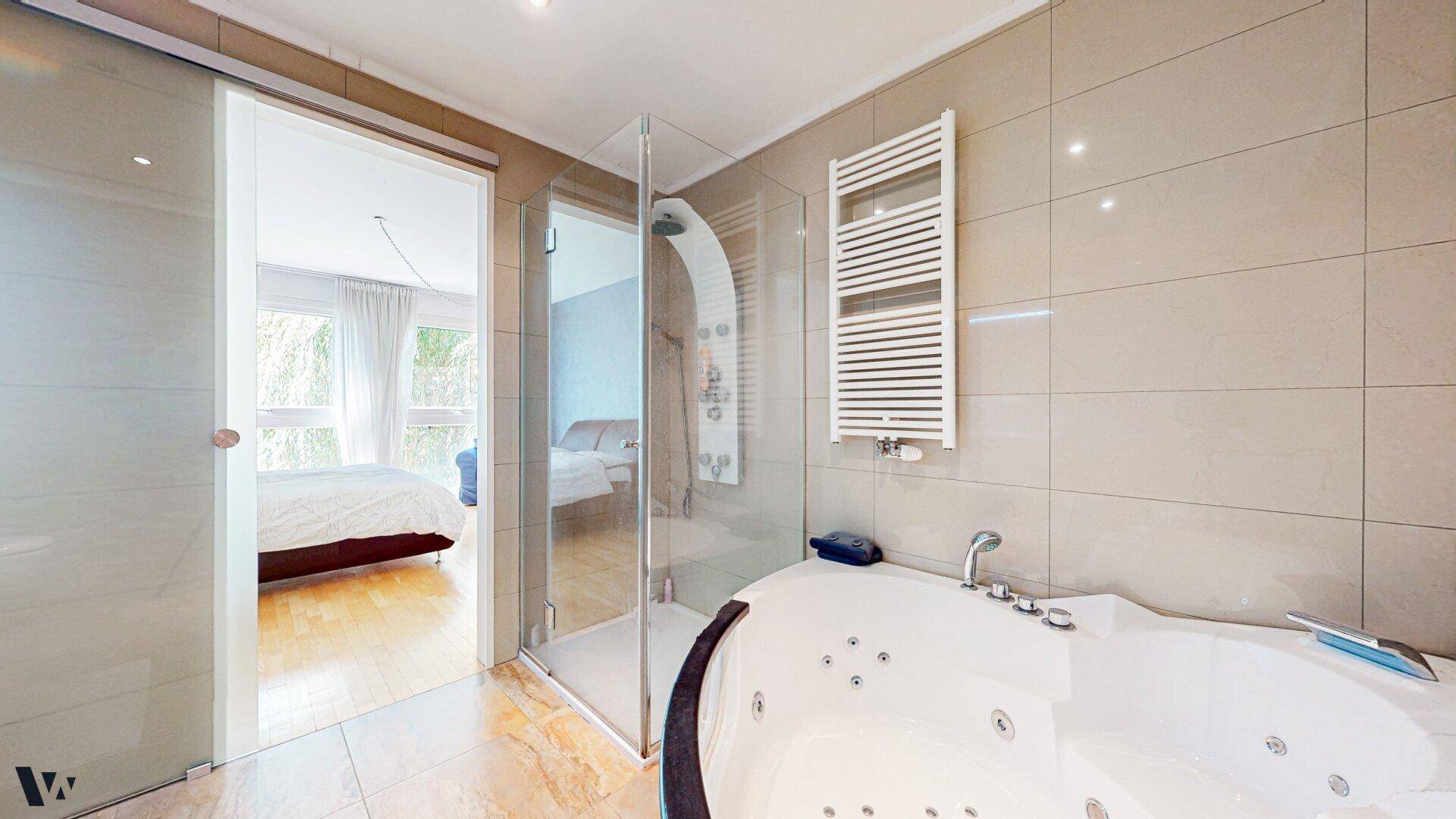 Modernes Badezimmer mit Whirlpool-Badewanne, Dusche und Zugang zum Schlafzimmer.