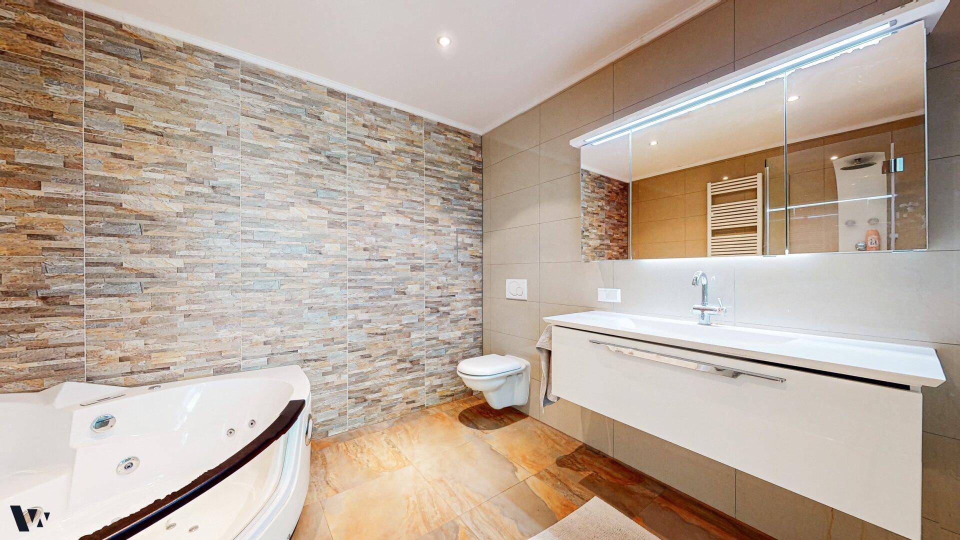 Elegantes Badezimmer mit Whirlpool, Waschtisch und dekorativer Steinwand.