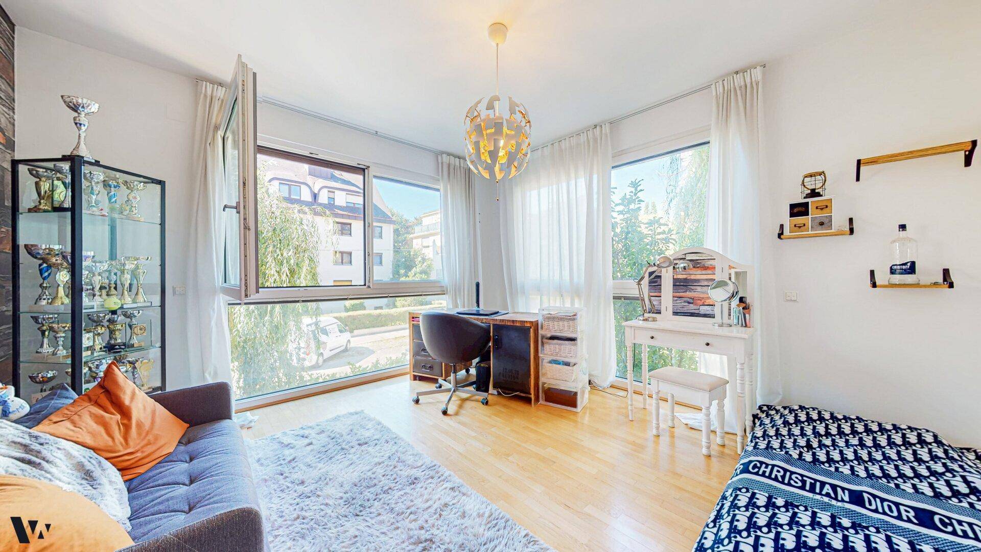 Helles Arbeitszimmer mit Holzboden, Schreibtisch und großen Fenstern mit Stadtblick.