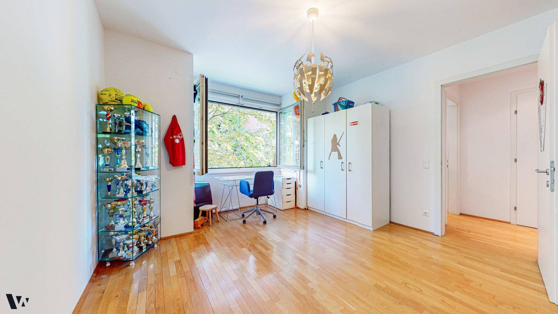 Kinderzimmer mit Holzboden, großem Fenster und Stauraum in weißen Schränken.