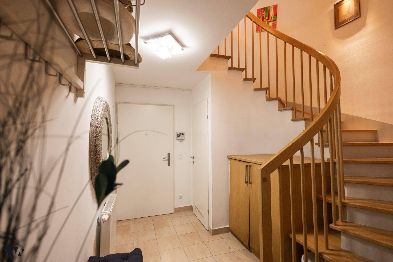 Eingangsbereich mit gefliestem Boden, Holztreppe und Garderobenschrank.
