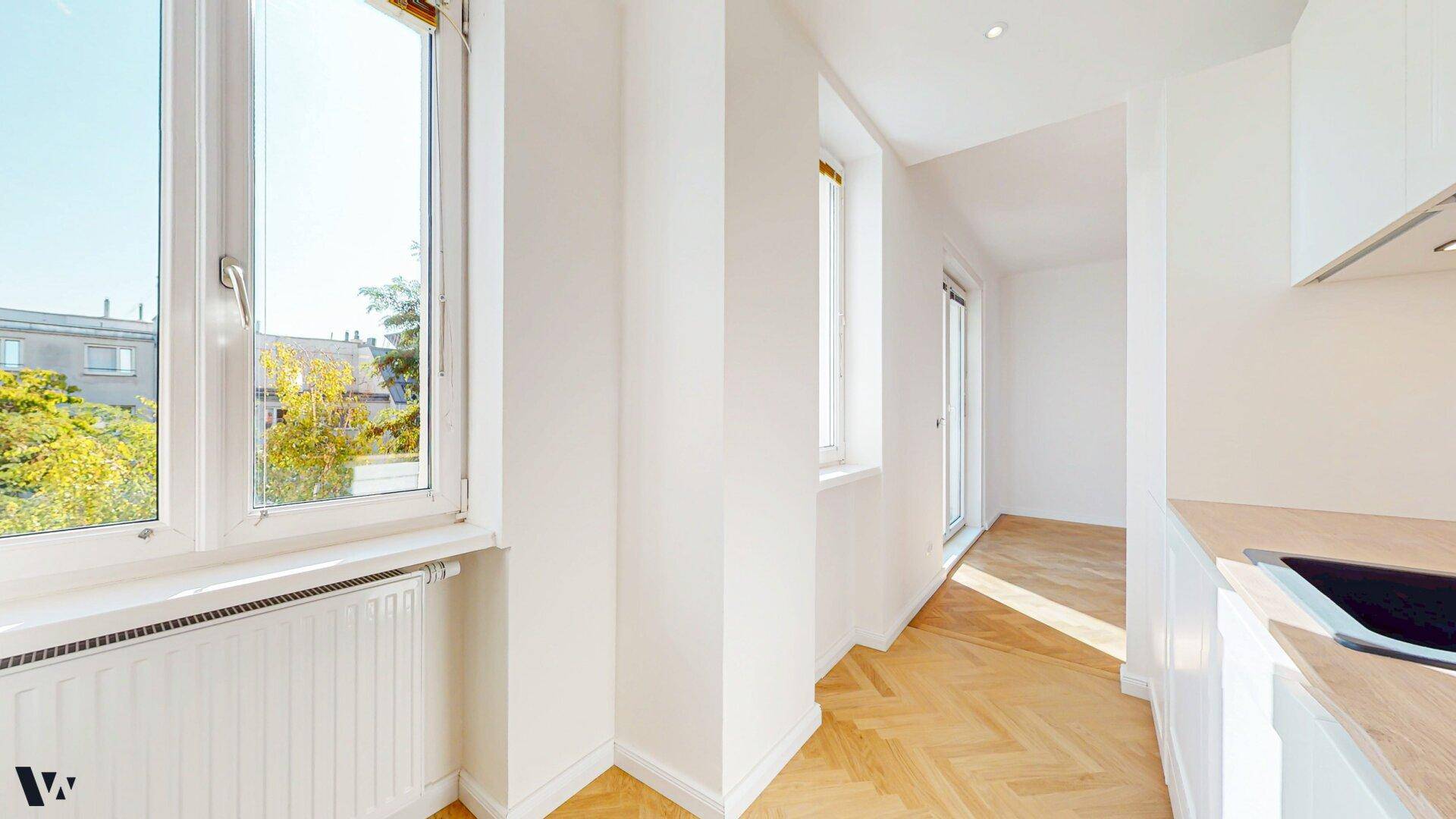 Heller Küchenbereich mit Fenster, Heizkörper und Blick in den angrenzenden Flur.