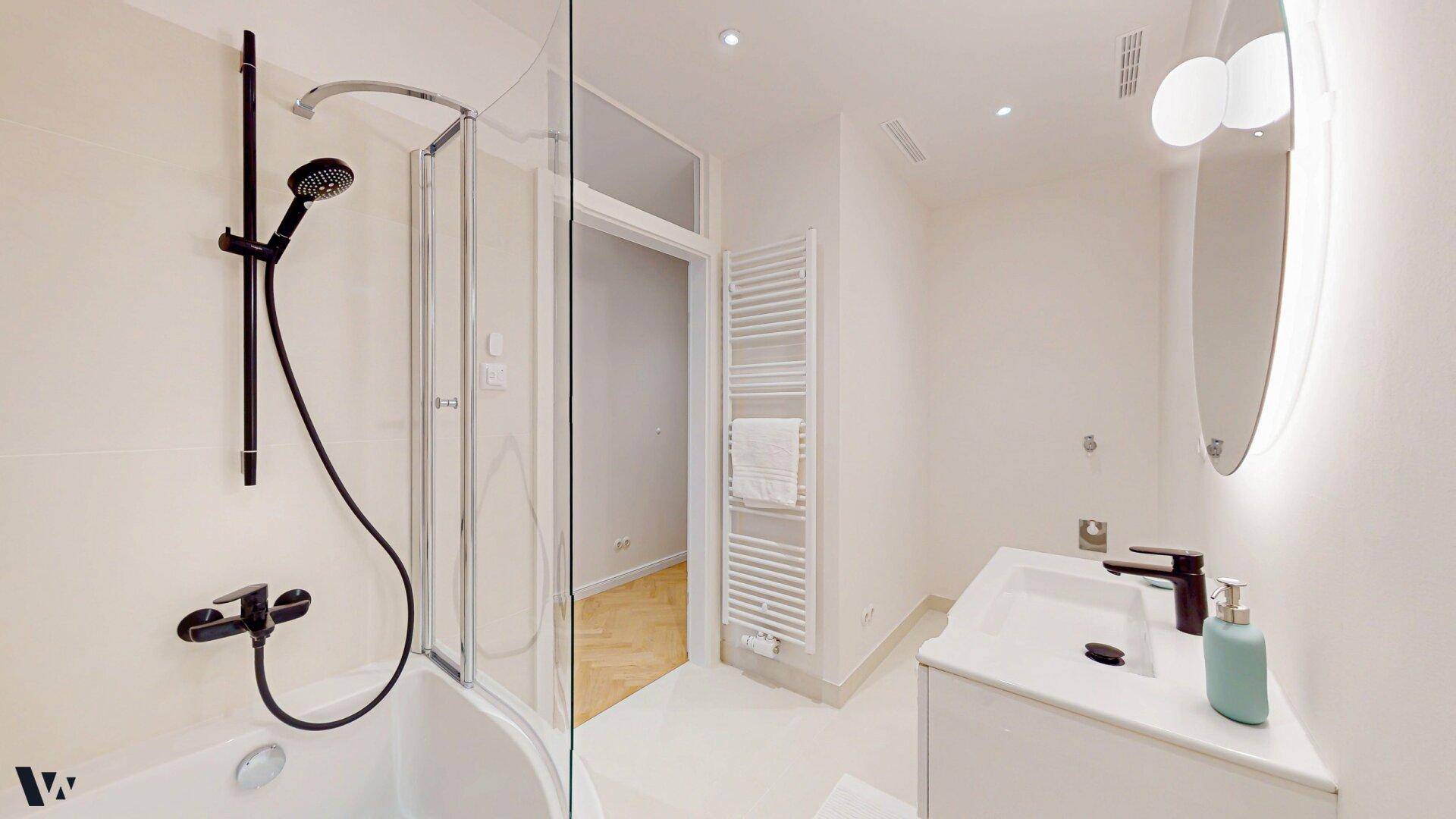 Modernes Badezimmer mit Badewanne, Dusche, Waschtisch und beleuchtetem Spiegel.