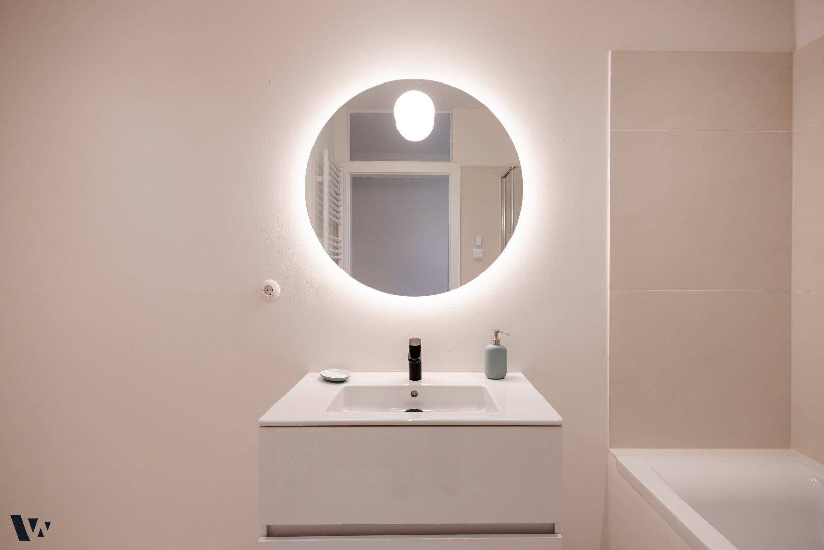 Detailaufnahme des modernen Waschtischs mit beleuchtetem Rundspiegel im Badezimmer.