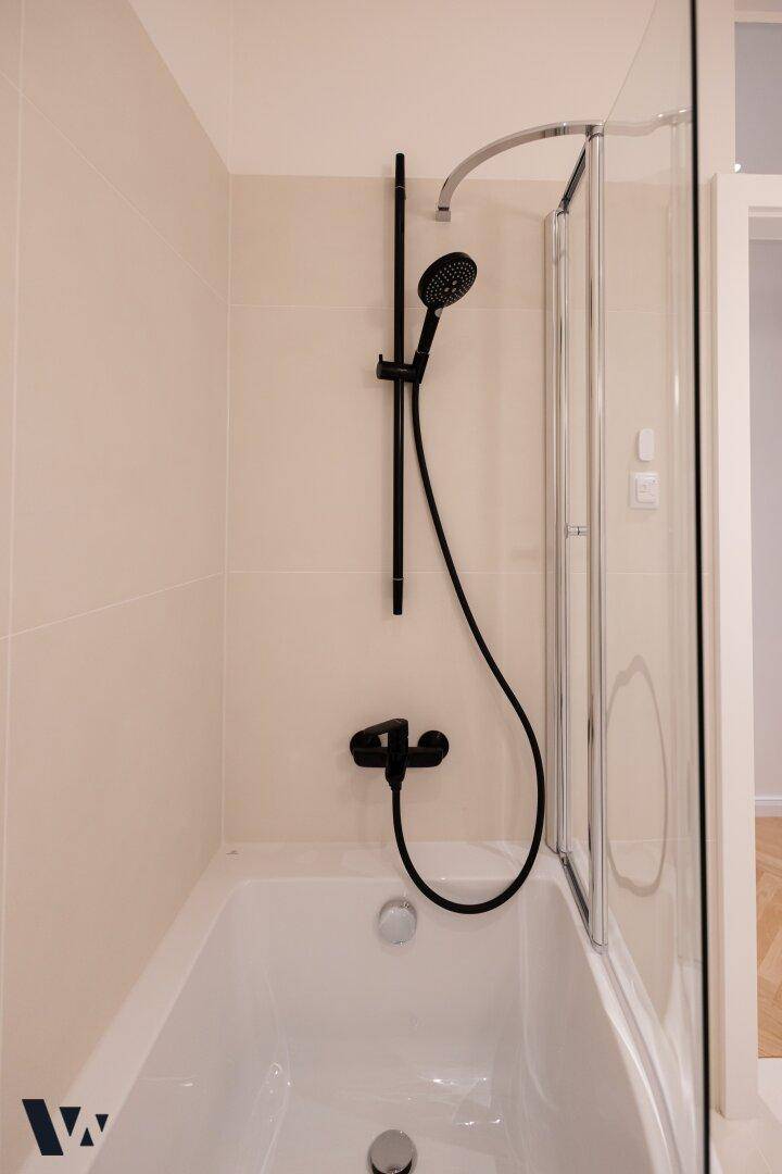 Badewanne mit moderner schwarzer Duscharmatur und Glasduschwand.