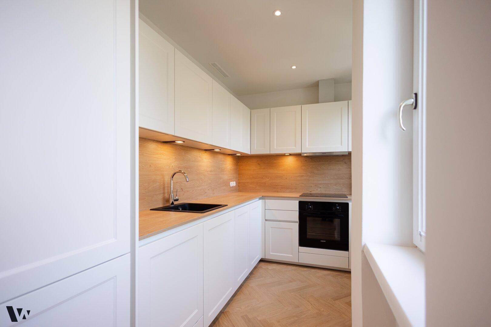 Moderne Küche mit weißen Schränken, Holz-Arbeitsplatten und integrierten Geräten.