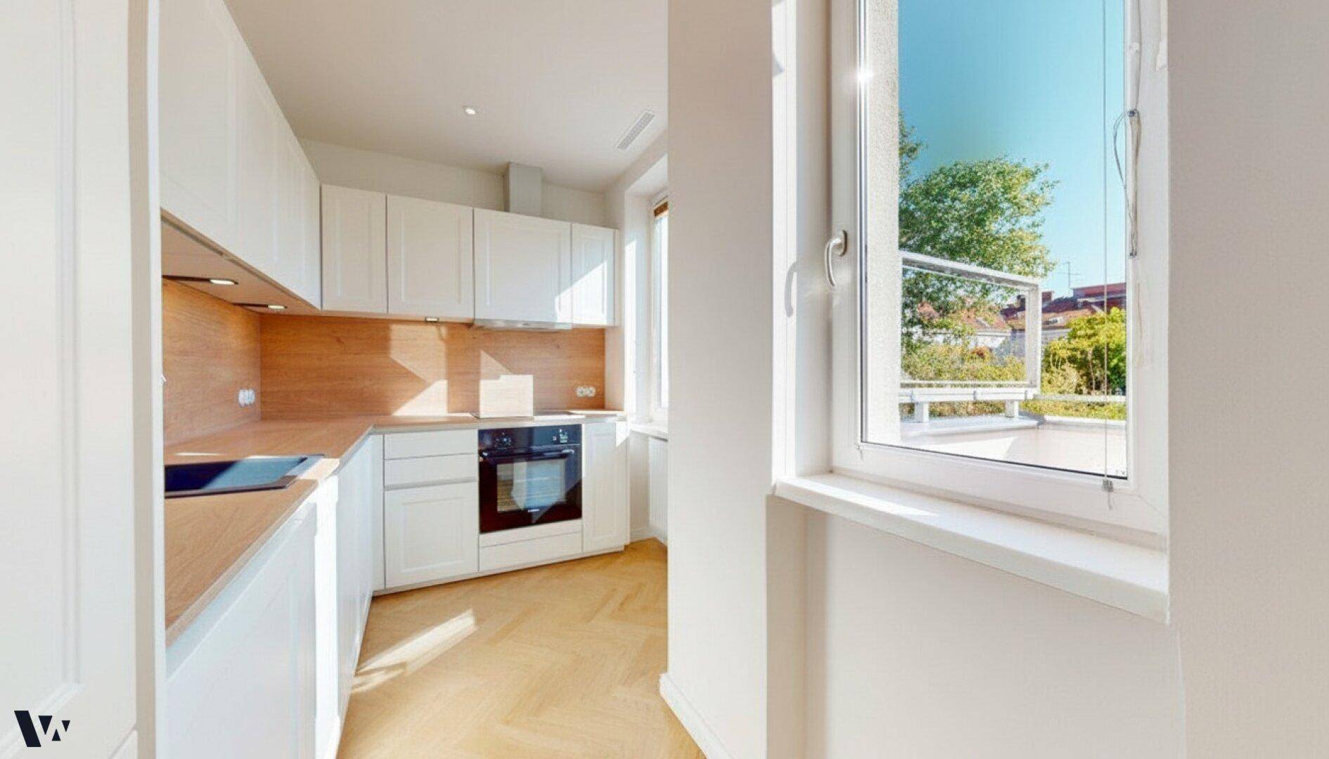 Helle Küche mit weißen Schränken, Holz-Arbeitsplatten und Fenster mit Blick ins Grüne.