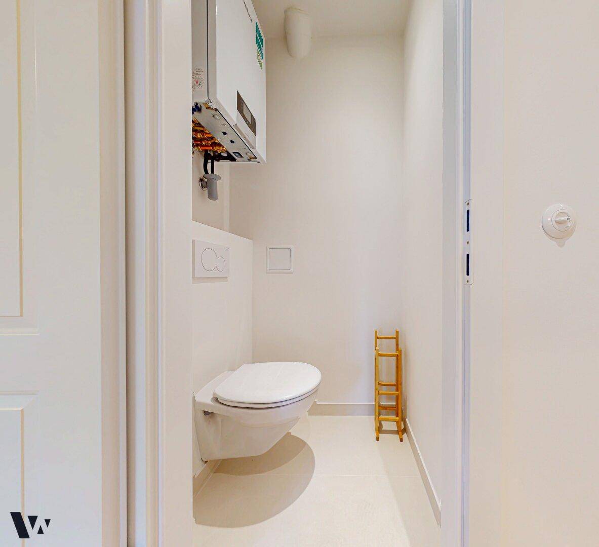 Separates WC mit wandhängender Toilette und hellen Fliesen.