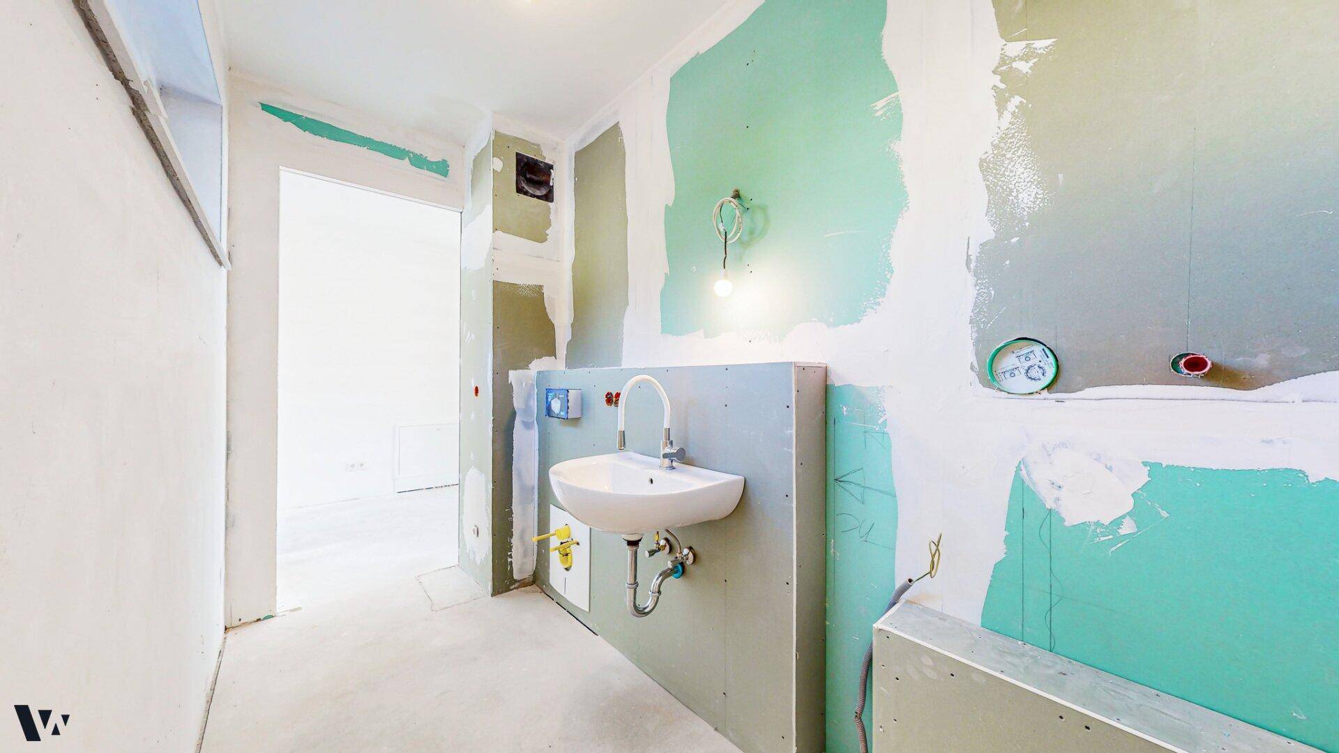 Badezimmer im Rohbau mit Waschbecken und vorbereiteten Installationen für weitere Sanitärobjekte.