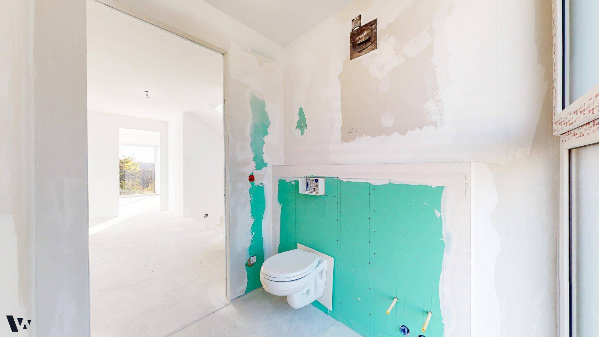 Unfertige Gästetoilette mit wandhängendem WC und vorbereiteten Installationen für die Endmontage.