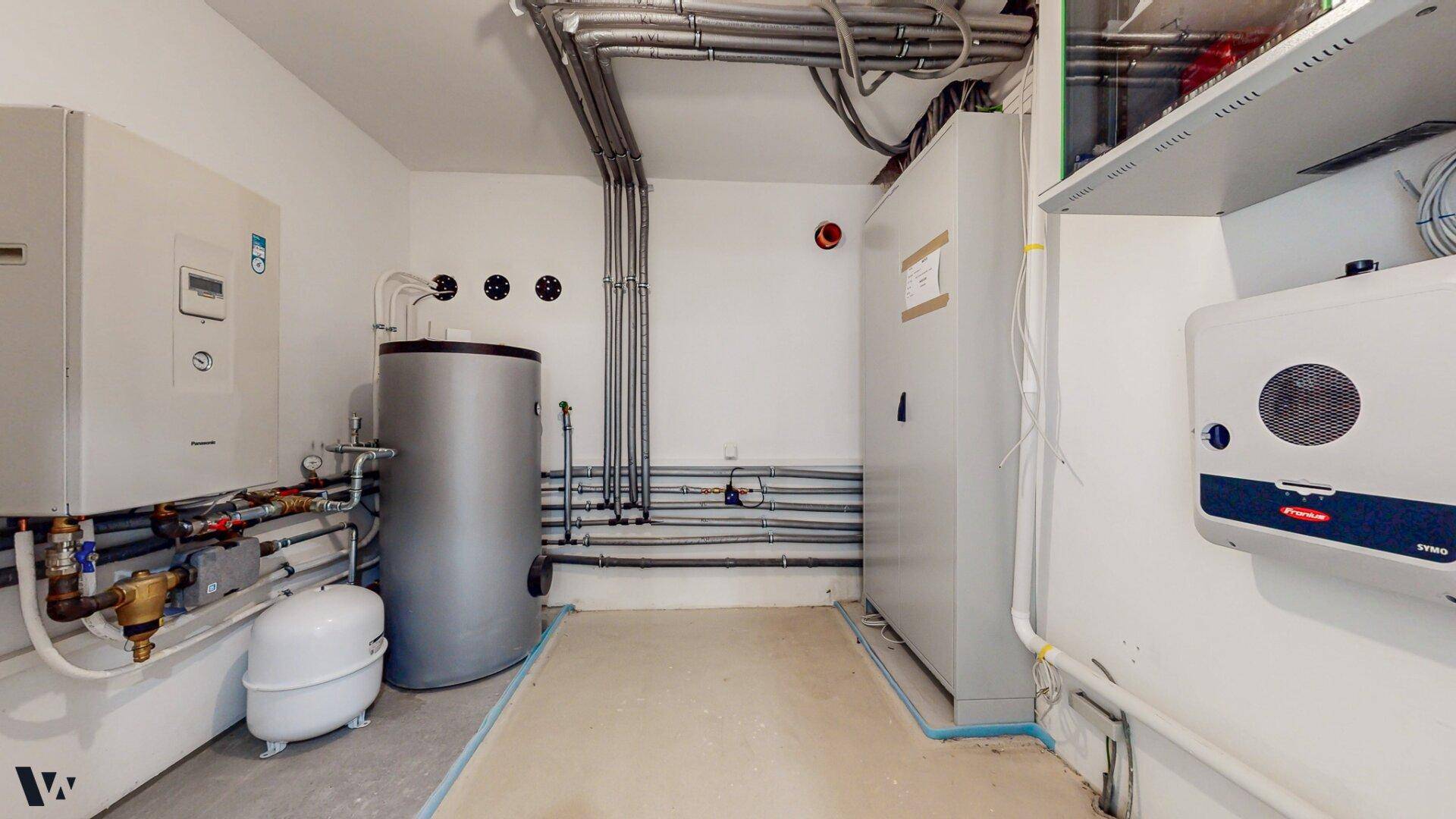 Technikraum mit Heizungsanlage, Warmwasserspeicher und weiteren Installationen, sauber und gut organisiert.
