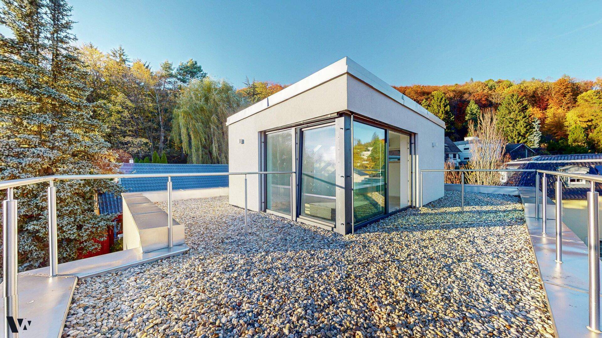 Dachterrasse mit Zugang zu einem verglasten Raum und Panoramablick auf die umliegende Landschaft.