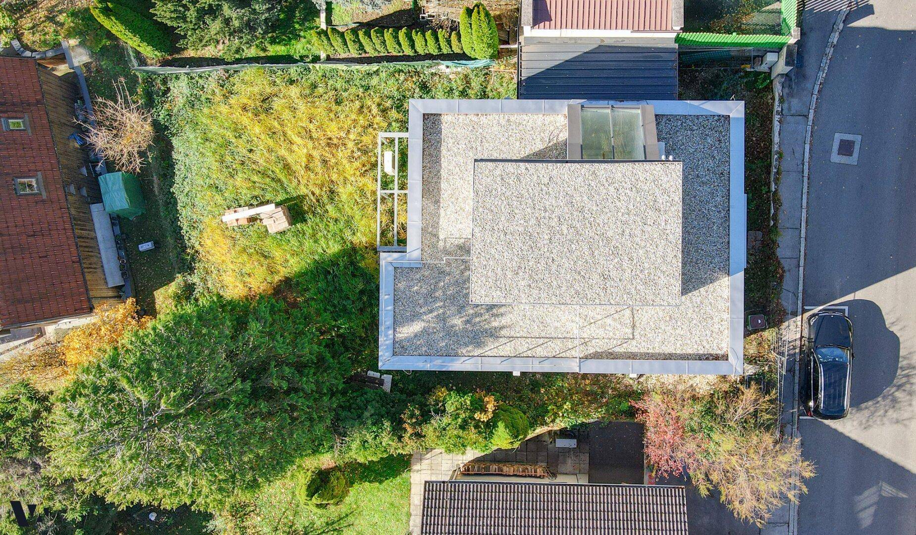 Luftaufnahme des modernen Hauses mit Kiesdach und umliegendem Gartenbereich in herbstlicher Landschaft.