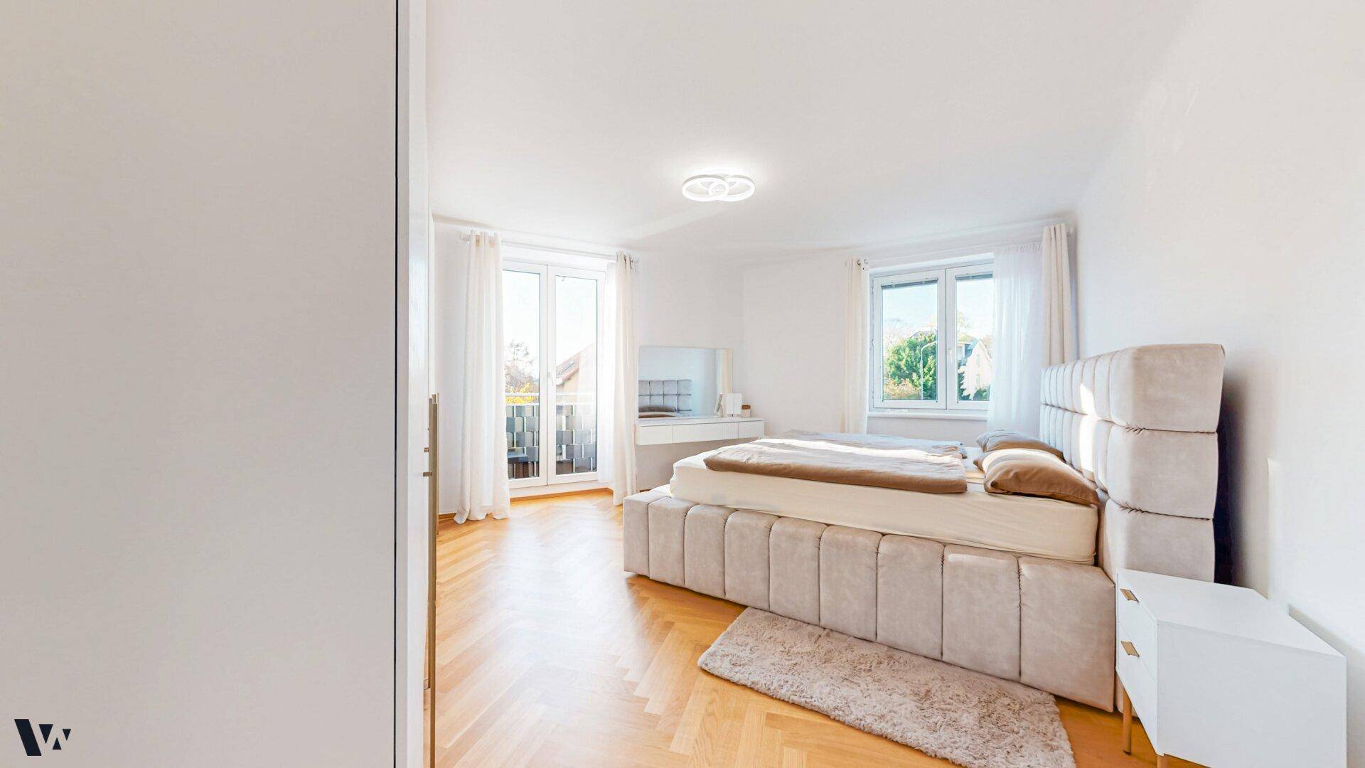 Helles Schlafzimmer mit großem Bett, Parkettboden und Zugang zum Balkon.