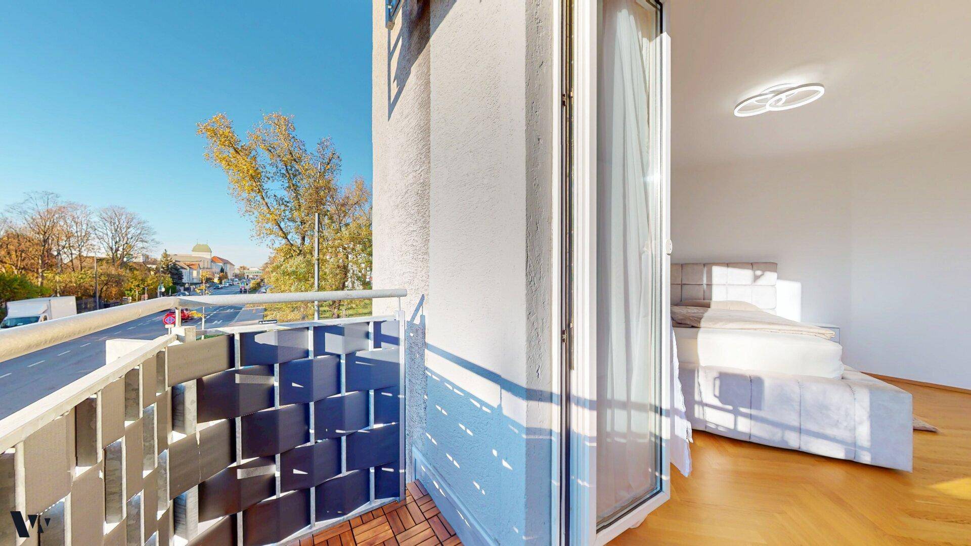 Sonniger Balkon mit Holzboden und Blick auf die Straße und umliegende Häuser.