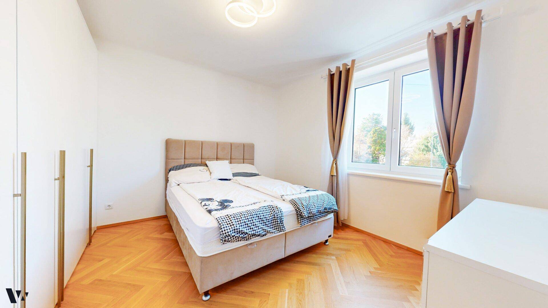 Gemütliches Schlafzimmer mit Doppelbett, Parkettboden und Fenster mit Vorhängen.