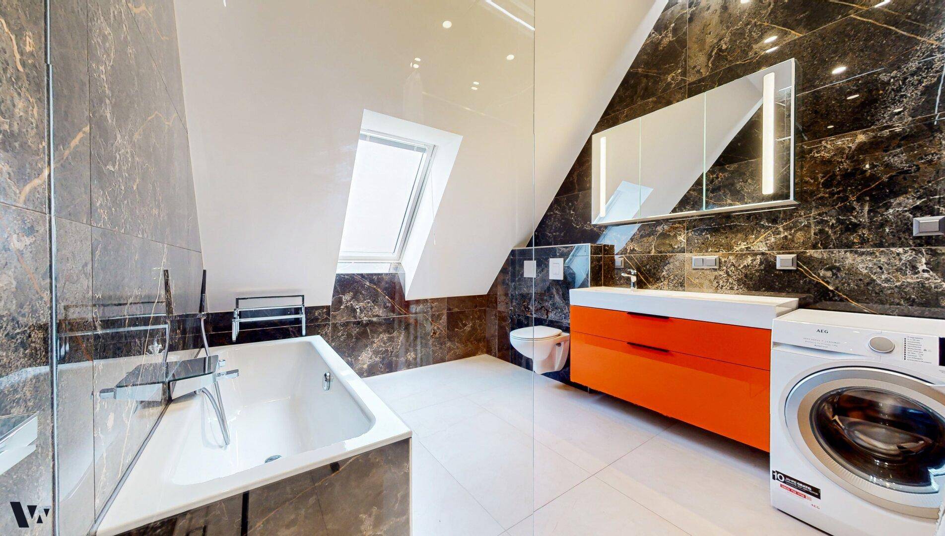 Modernes Badezimmer mit dunklen Marmorfliesen, Badewanne und orangefarbenem Waschtisch.