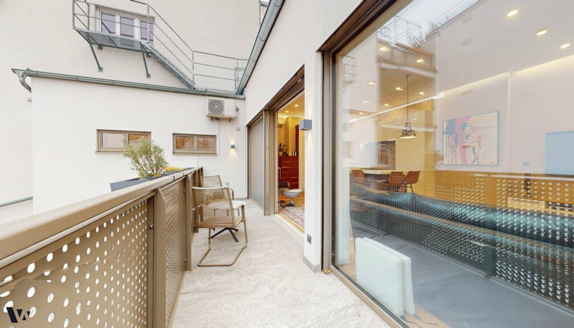Balkon mit Outdoor-Möbeln und großen Glasfronten, die den Blick ins Innere freigeben.