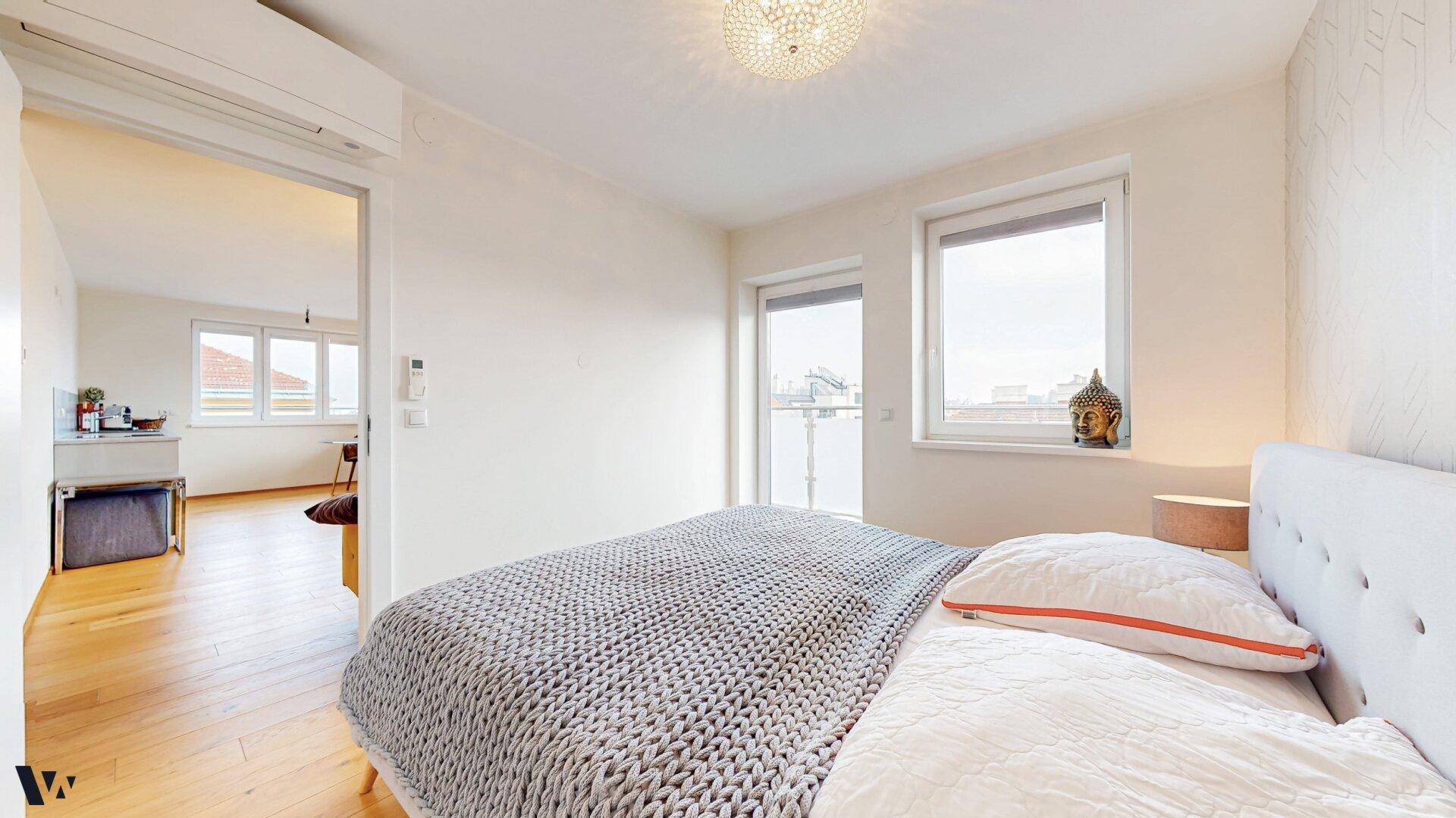 Helles Schlafzimmer mit Holzboden und Zugang zum Balkon, verbunden mit dem offenen Wohnbereich.