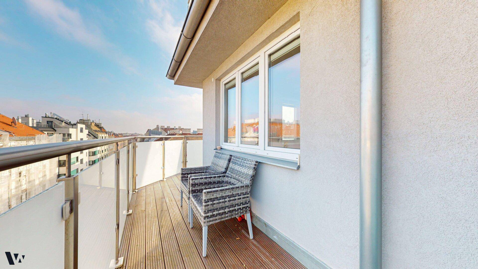 Gemütlicher Sitzbereich auf dem Balkon mit Blick auf die umliegenden Gebäude und den Himmel.