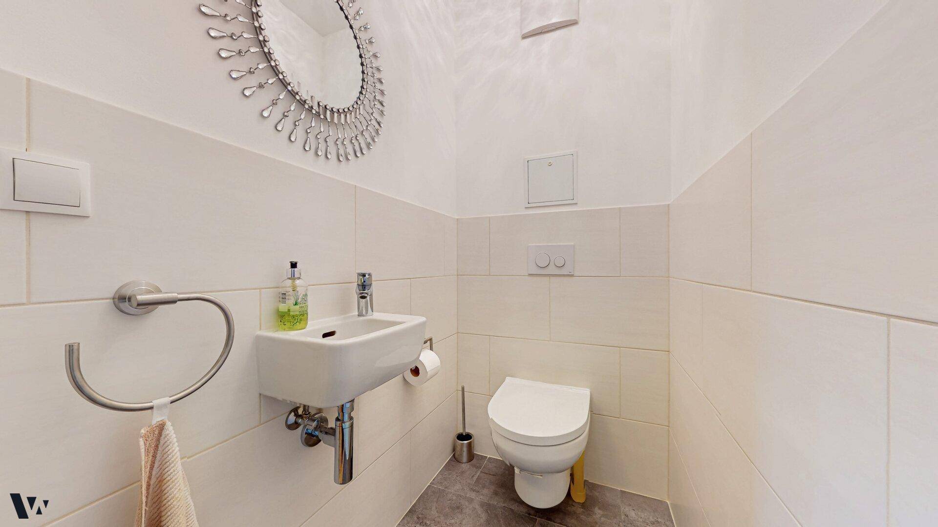 Separates Gäste-WC mit Wand-WC, kleinem Waschbecken und dekorativem Spiegel.