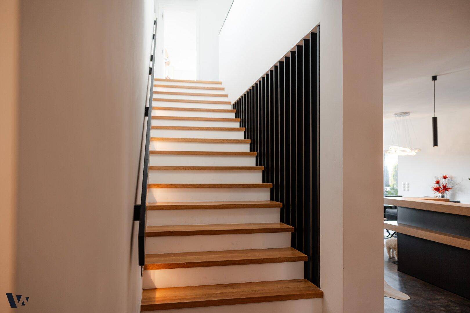 Moderne Holztreppe mit schwarzem Geländer, die die verschiedenen Ebenen des Hauses verbindet.