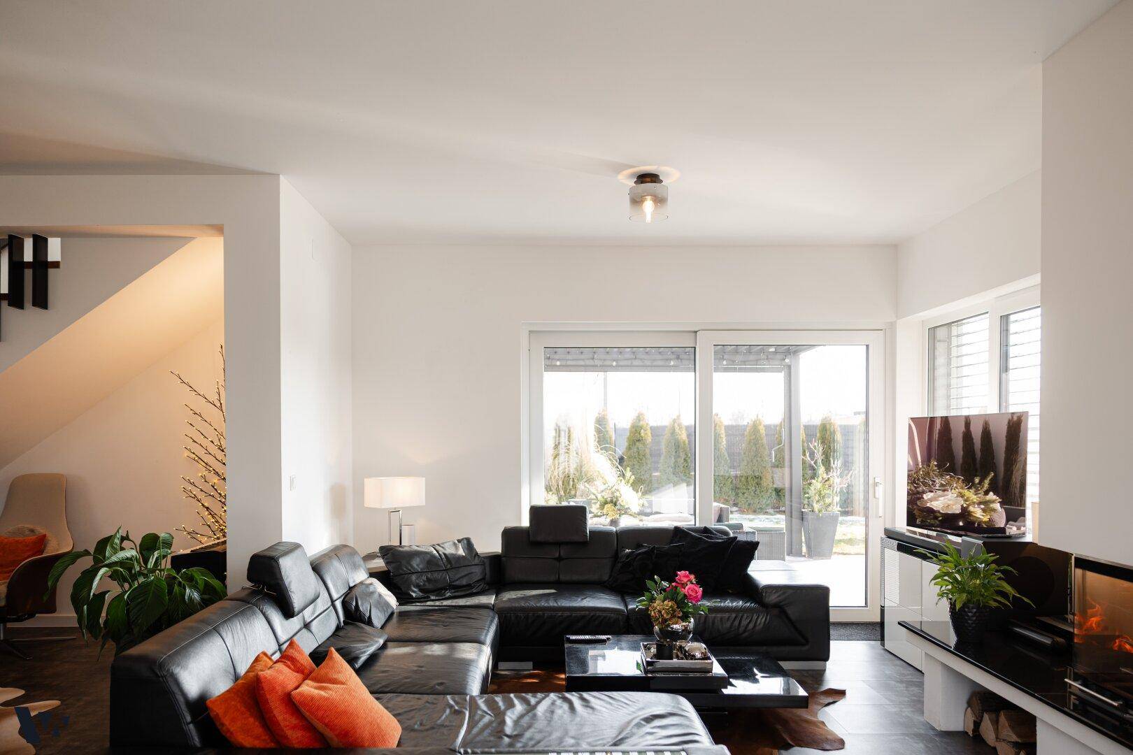 Gemütliches Wohnzimmer mit großem Ledersofa, Kamin und Zugang zur Terrasse durch Schiebetüren.