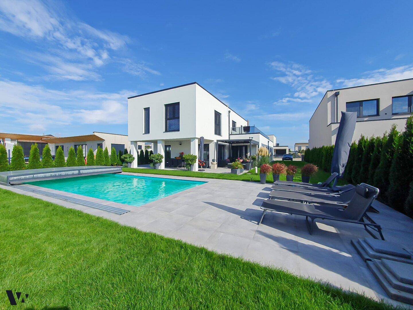 Weitläufiger Garten mit modernem Pool, Liegestühlen und gepflegter Rasenfläche vor dem Haus.